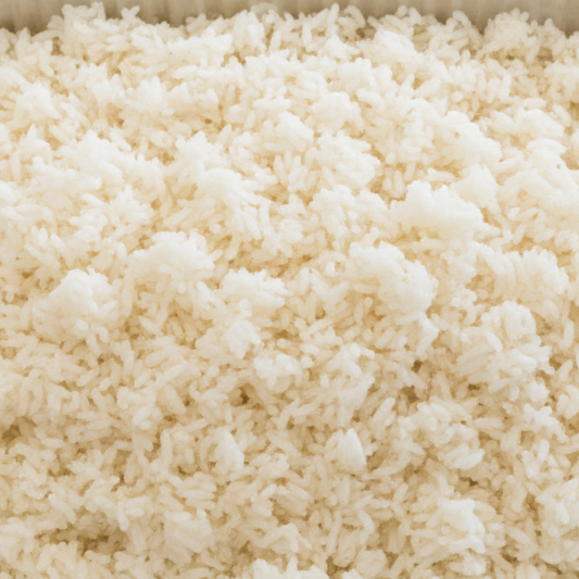 High-angle shot of a single rectangular stainless steel chafing dish filled with fluffy white long-grain steamed rice. The dish is set on a table in a brightly lit modern office lounge environment.